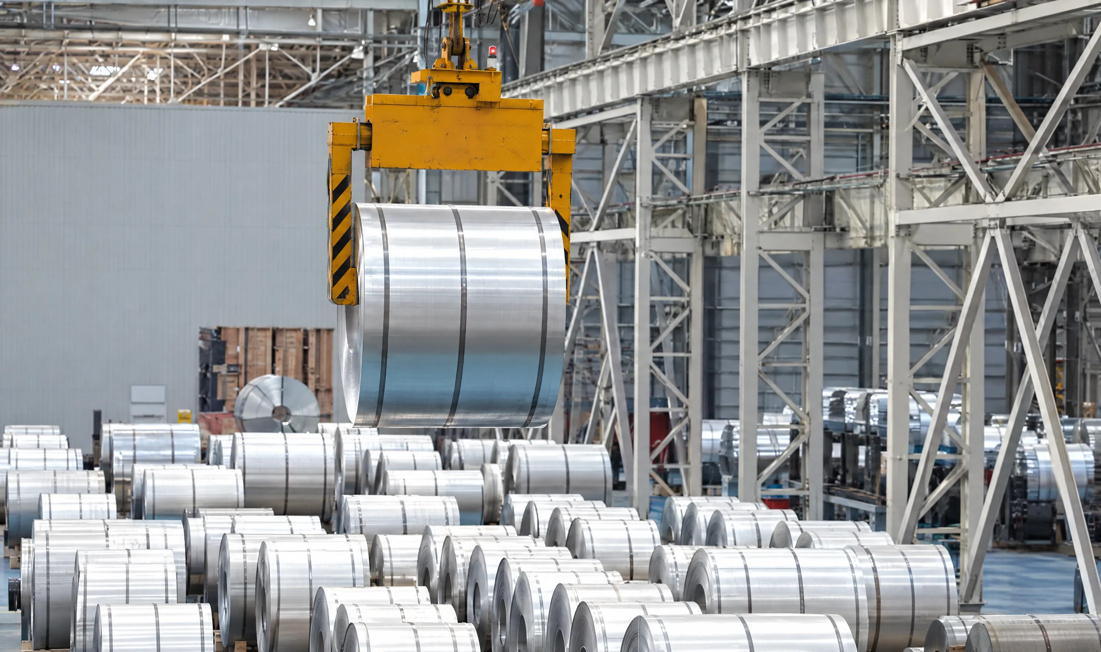 Kran hebt ein blankes Coil in einer Halle über Reihen weiterer Coils